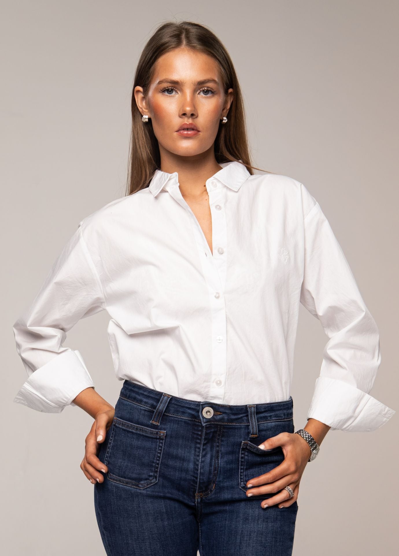 Woman wearing a white shirt and blue jeans against a neutral background
