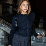 A woman wearing a dark navy fuzzy knit cardigan and a dark navy pinstriped skirt, standing on stone stairs at night with a black handbag.