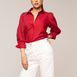 Woman wearing a red blouse and white pants against a plain background