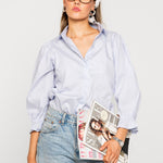 Woman wearing a blue shirt, jeans, and glasses holding a magazine against a white background