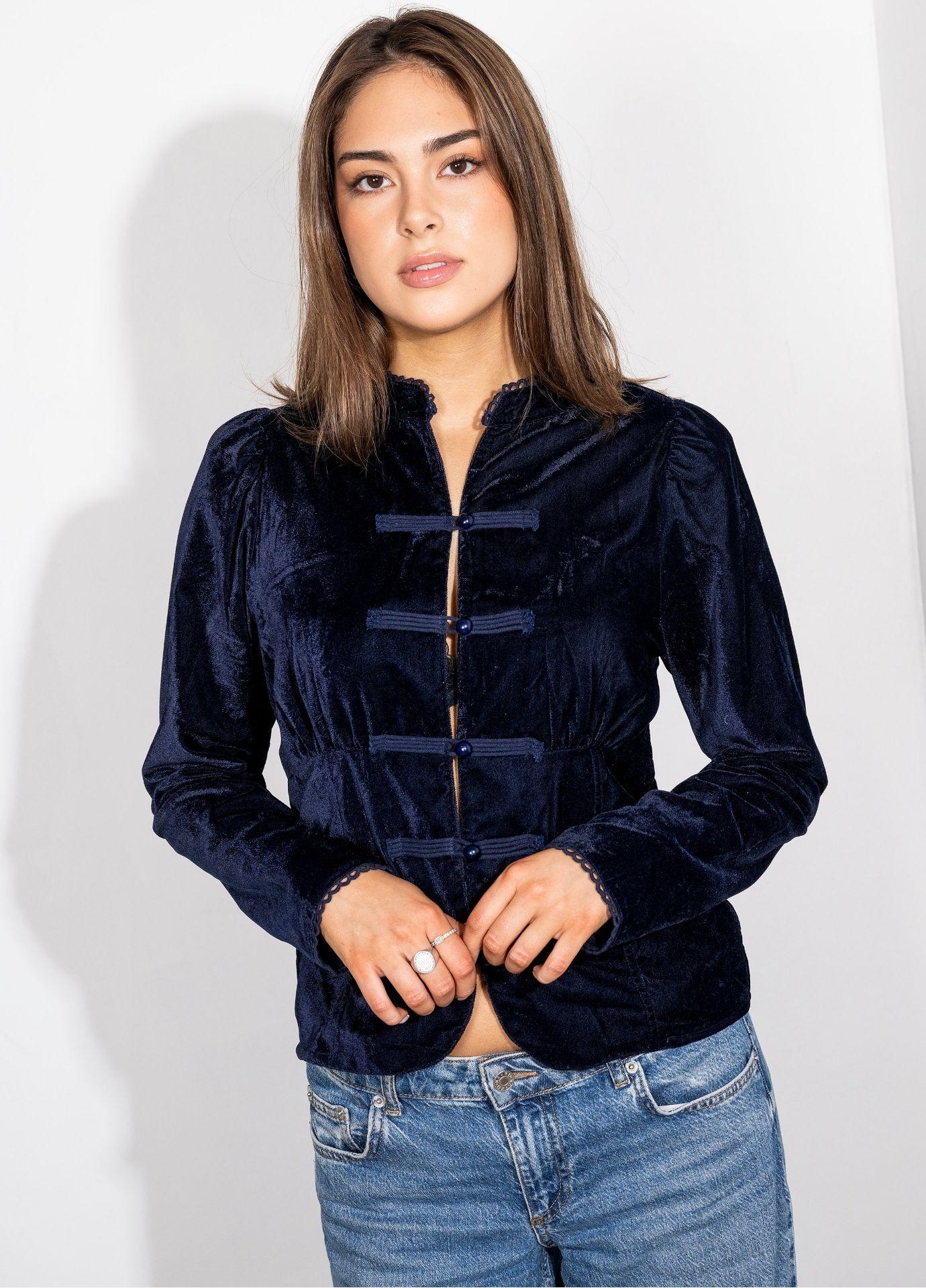 Amora Blouse Velvet Blue Sapphire in a close front view with the model's hands resting at the hem, showing the gathered waist seams, the gently curved hem and the lace trimmed cuffs. Styled with light blue jeans.
