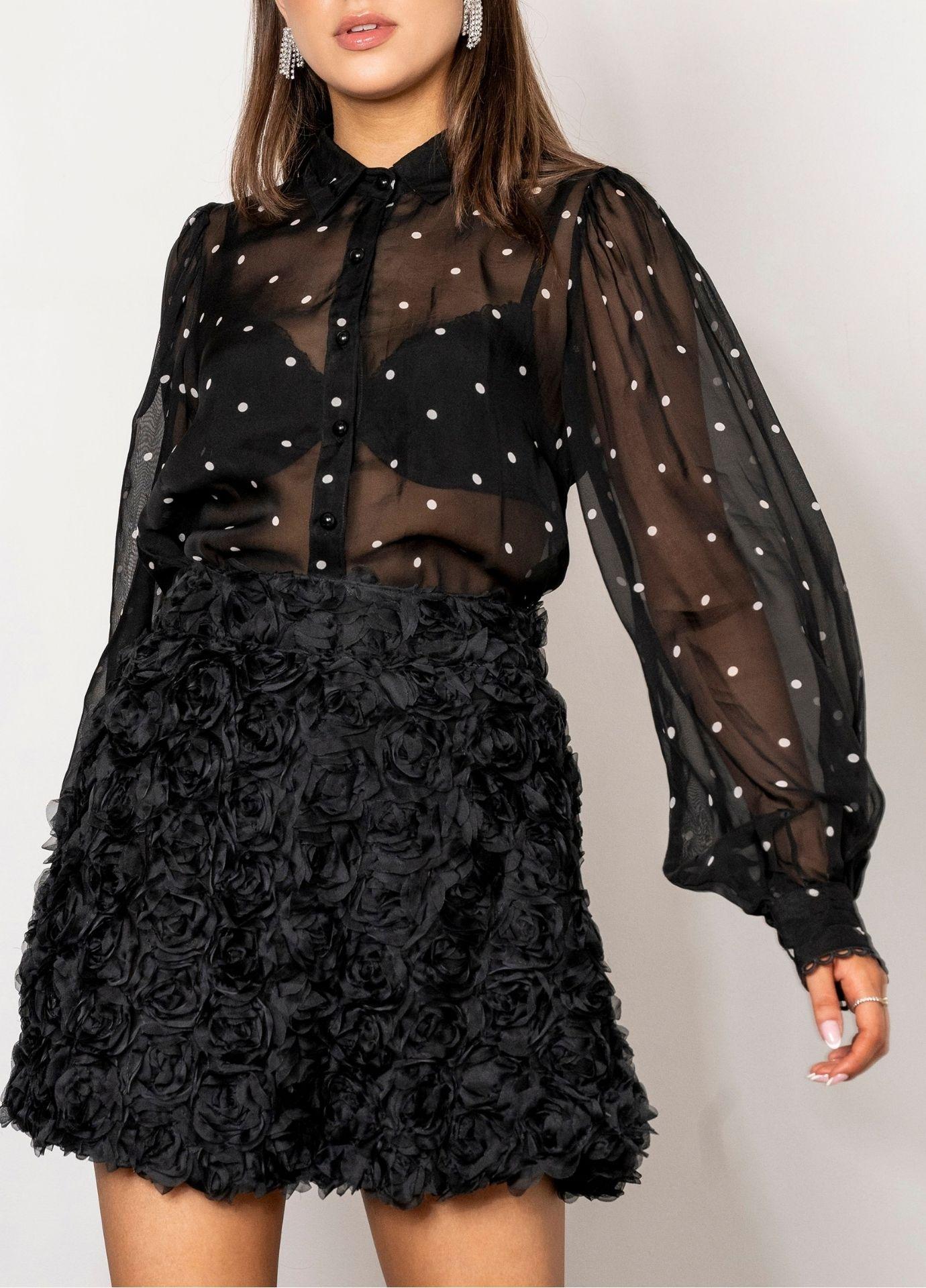 Anaya Blouse Black Pearl in a close front view with the arms relaxed, showing the full balloon sleeves gathered into lace trimmed cuffs. Styled with a black rosette mini skirt against a white background.