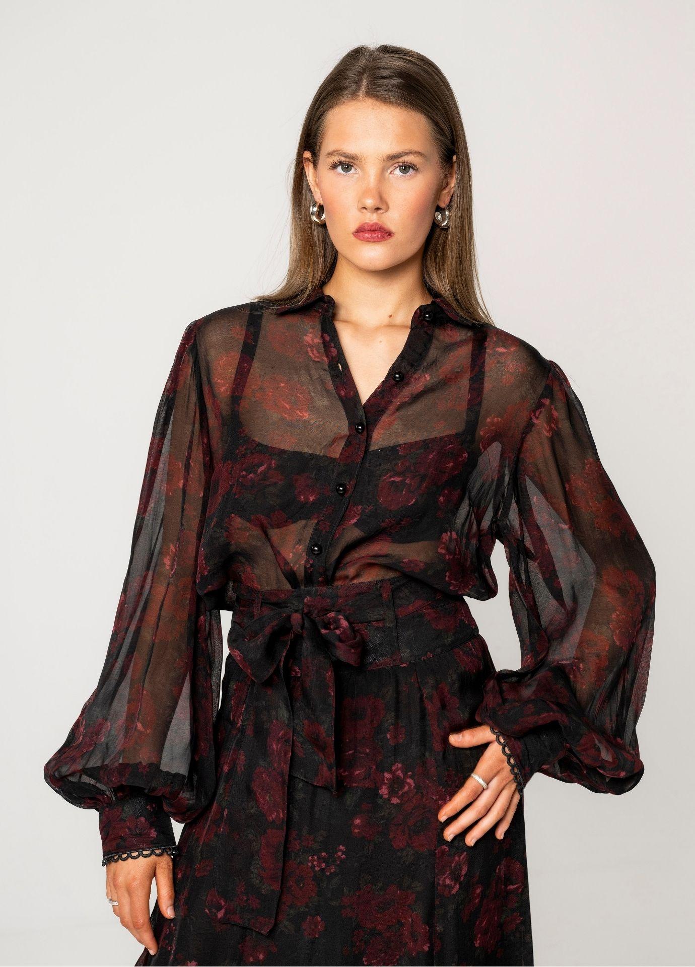 Anaya Blouse Black Romance in a close front view, showing the classic collar, the button front and the dark red roses printed on sheer black fabric. The matching skirt ties with a bow at the waist.
