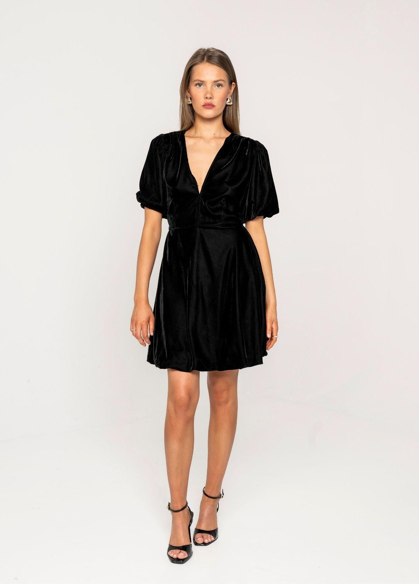 Blake Dress Velvet Black in a full length front view in a light grey studio, the black velvet mini dress styled with black strappy heels.