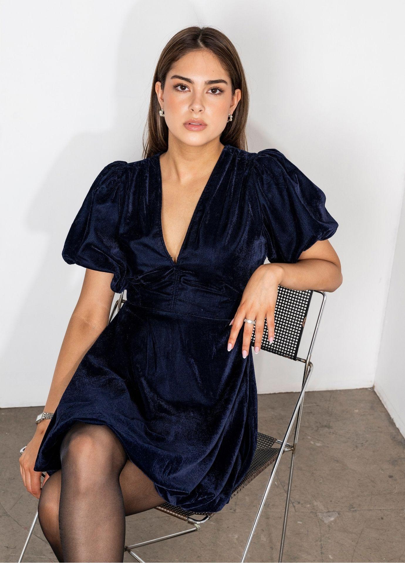 Blake Dress Velvet Blue Sapphire with the model seated on a chair, a front view of the V-neckline and the balloon skirt in deep blue velvet.