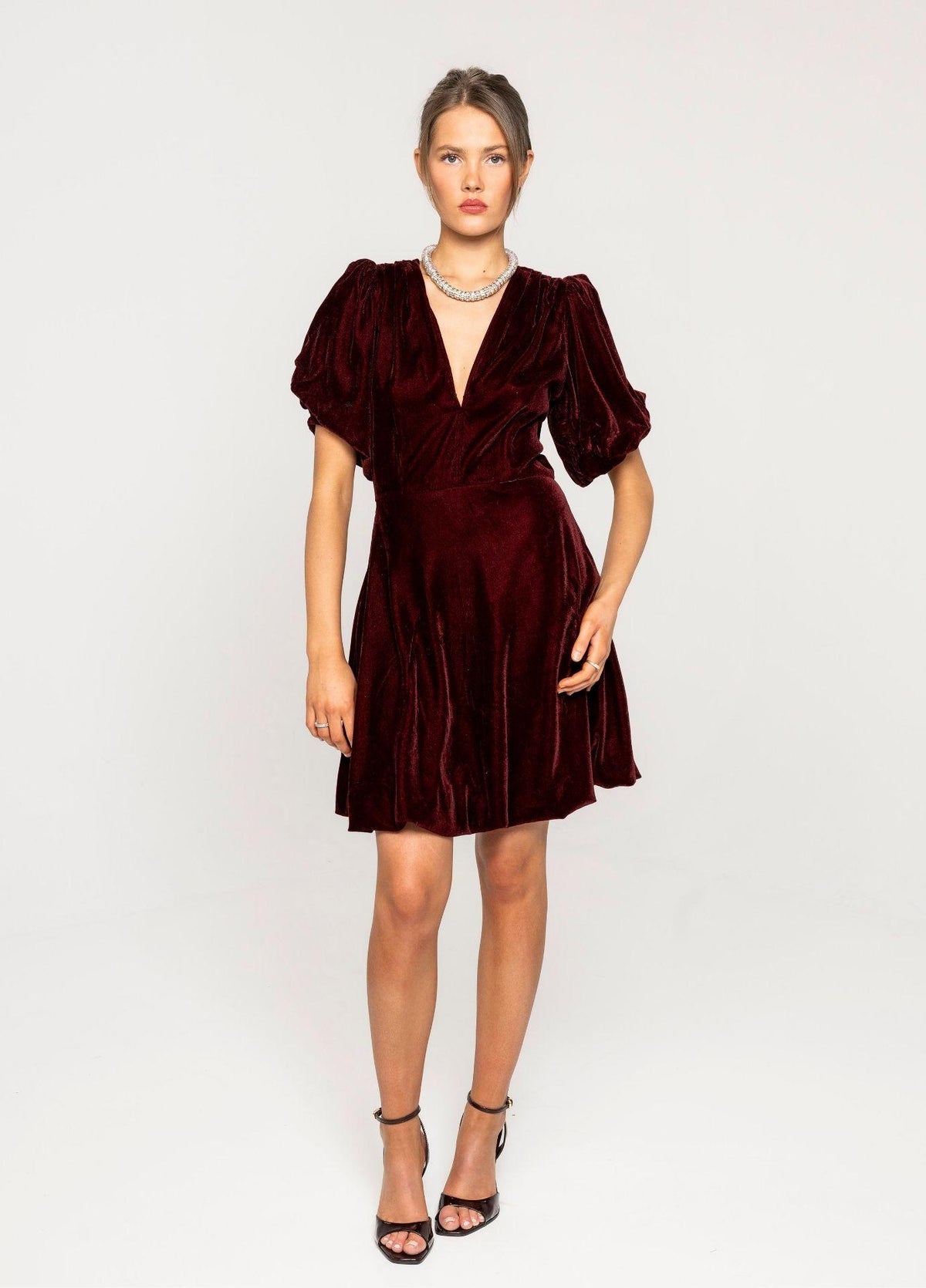 Blake Dress Velvet Bordeaux in a full length studio view, showing the balloon skirt and the short puff sleeves with black strappy heels against a light grey background.