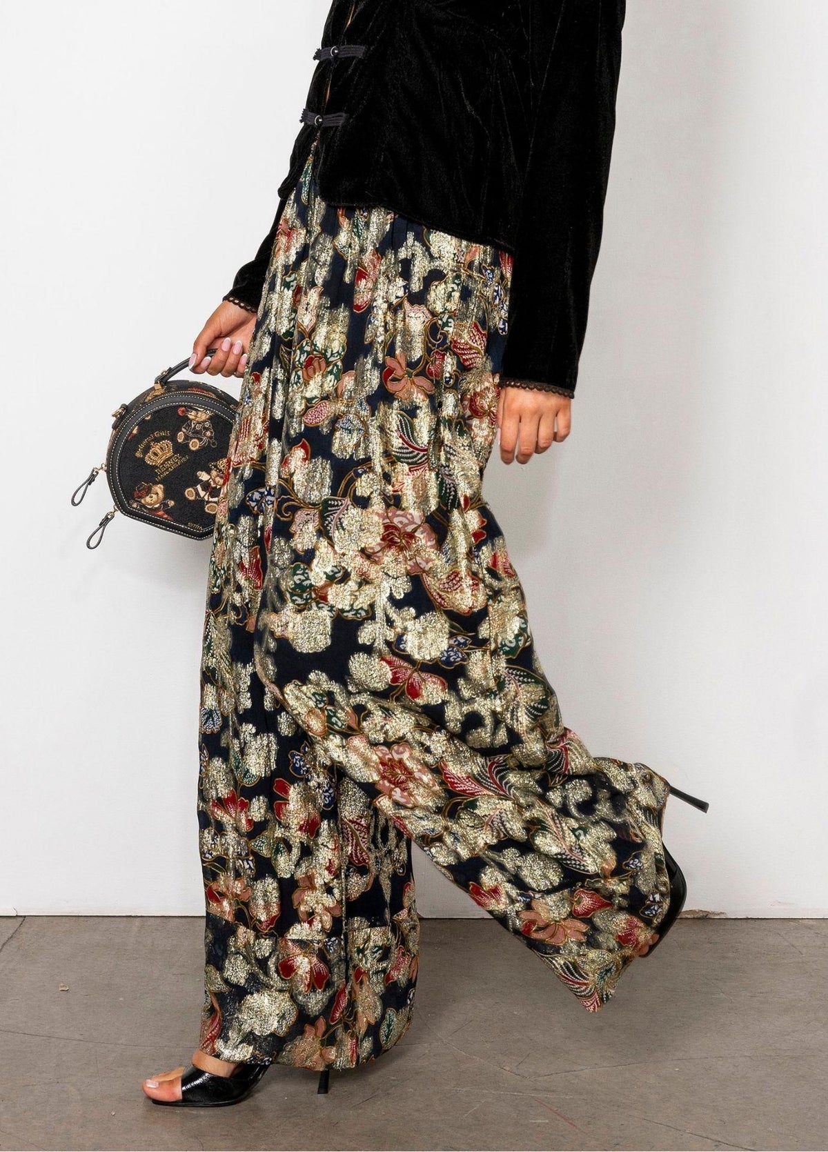 Elida Pant Golden Night in a side view in motion, showing the fluid wide leg and the gold and rust toned florals on a black base.