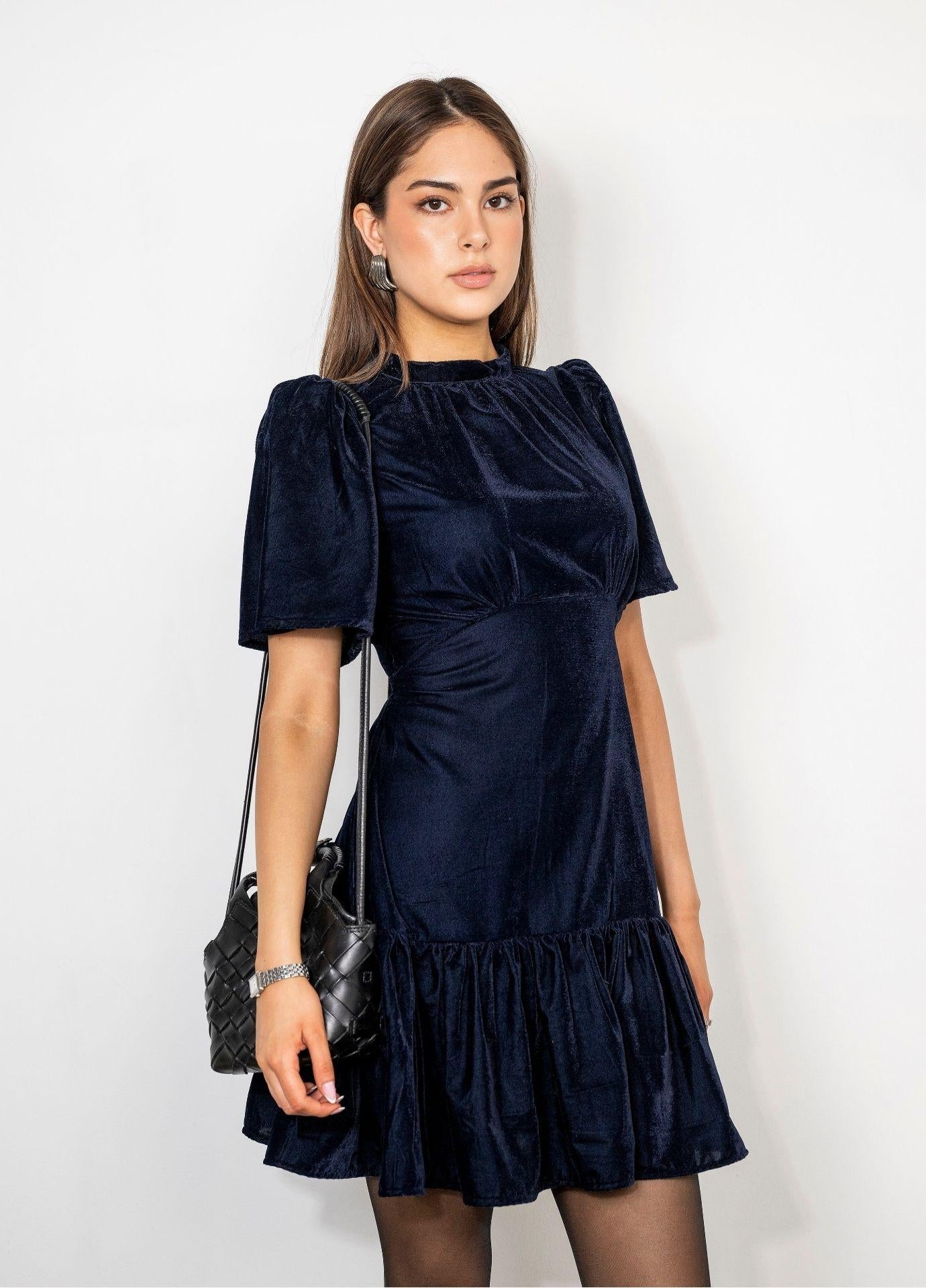 Jolie Dress Velvet Blue Sapphire in a front view with a black shoulder bag, showing the fitted bodice and the gathered seam under the bust.