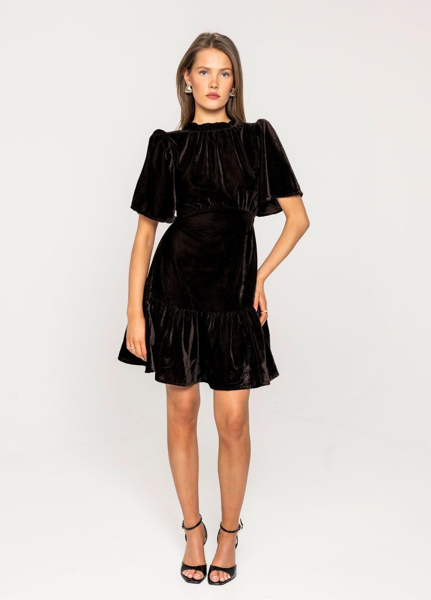 Jolie Dress Velvet Toffee in a studio view with one hand on the hip, showing the short flared sleeves of the brown velvet dress.