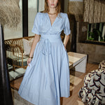 Woman in a light blue striped cotton dress with puff sleeves, elastic band in the back of the waist and a full skirt. Perfect summer dress that can be dressed up or down.