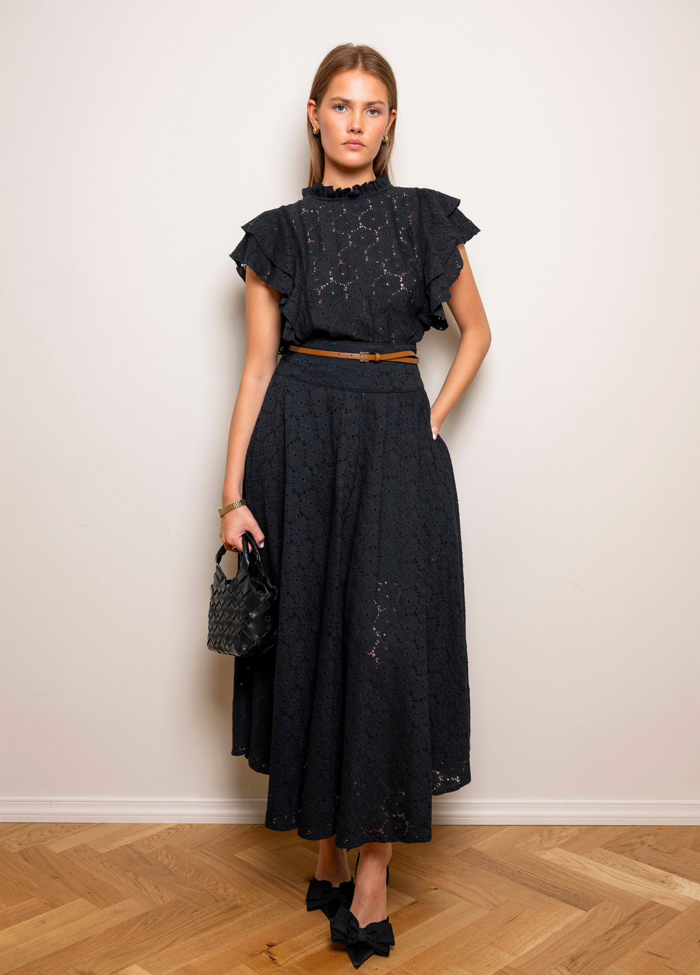 Astrid Skirt Black Lace in a full length view showing the volume of the midi skirt, styled with a matching black top against a beige wall.