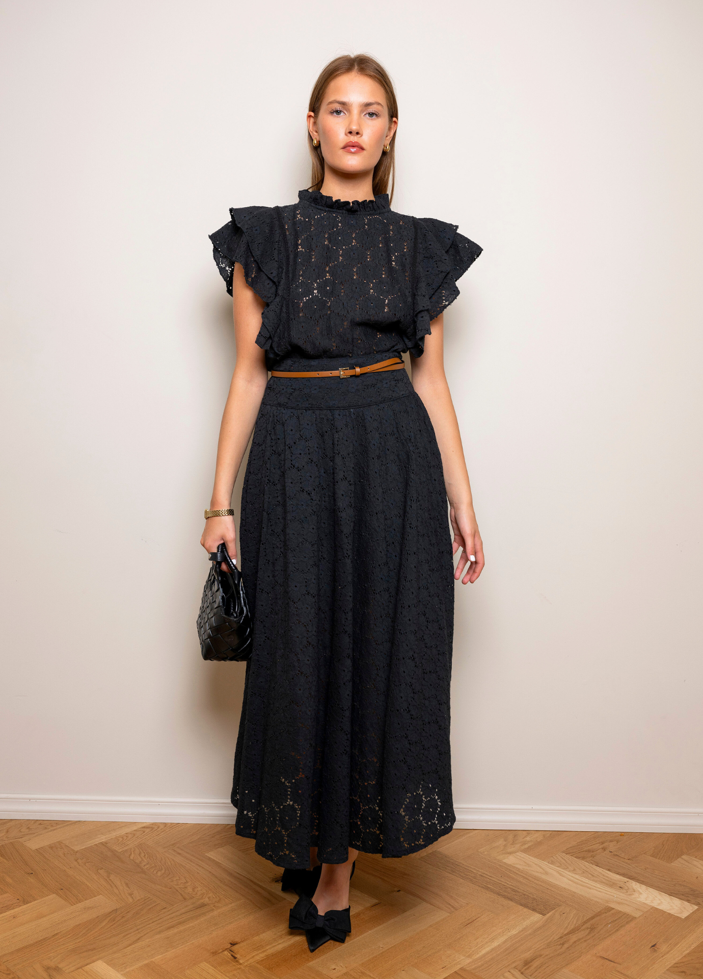 Astrid Skirt Black Lace with a thin black belt at the waist, full length front view with black heels on a herringbone wooden floor.