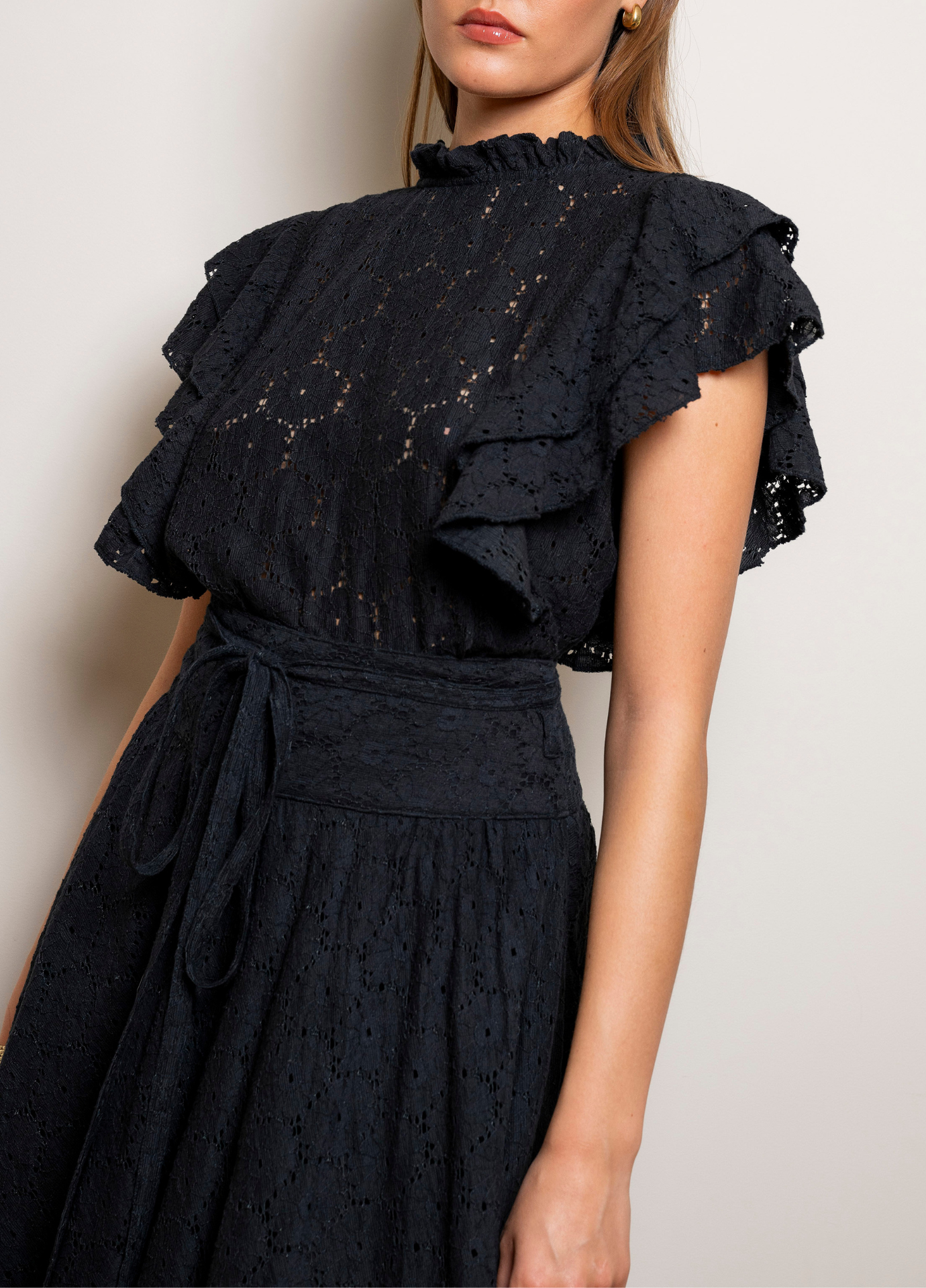 Astrid Skirt Black Lace in a close view of the belted waist and the embroidered black lace, worn with a black top with ruffled sleeves.