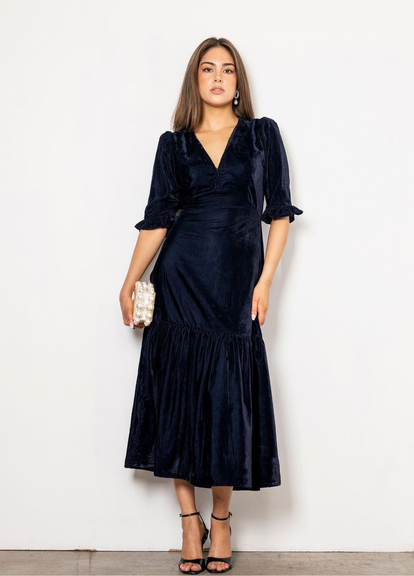 Ophelia Dress Velvet Blue Sapphire in a full length front view, showing the V-neckline, the fitted shape and the flounced hem against a white wall.