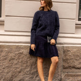 A woman wearing a fuzzy dark navy blue button-front cardigan sweater, standing outdoors against a light-colored building wall.